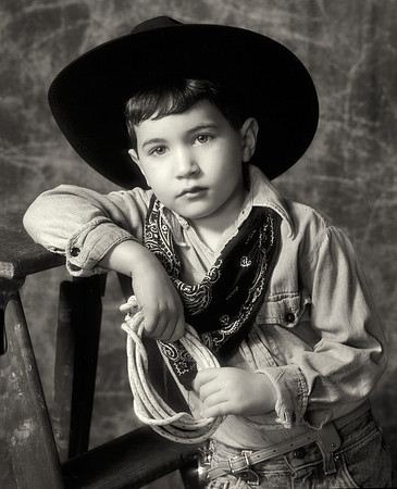 Classic studio portrait, black & white, closeup of a young cowboy with hat, kerchief, and rope.