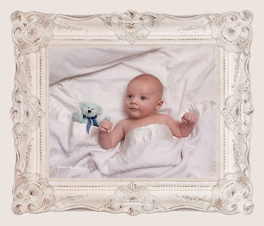 baby boy with teddy bear resting in white sheets on bed in white ornate frame