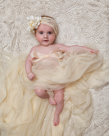 Baby Girl is draped in cream colored chiffon with a lace and flower headpiece.